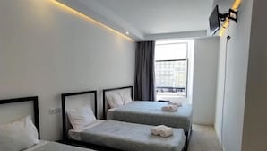Een moderne hotelkamer met twee enkele bedden, een groot raam en een flatscreen televisie aan de muur.