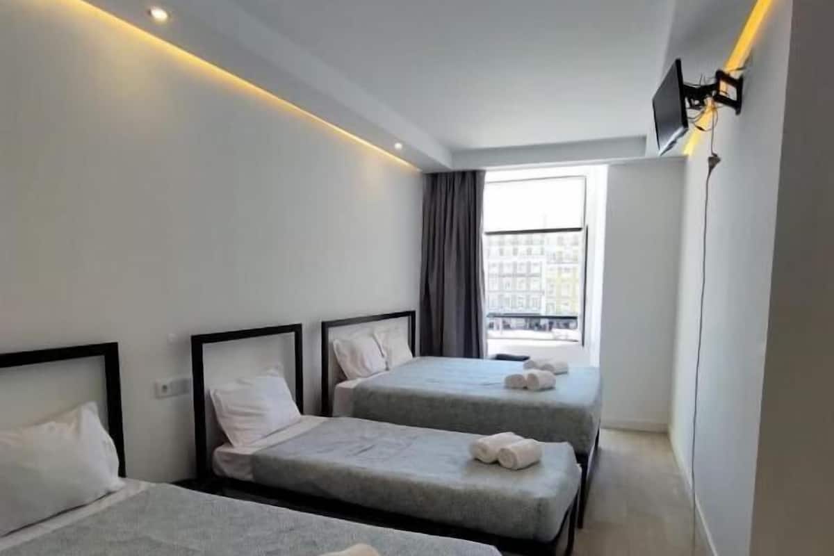 Une chambre d’hôtel moderne équipée de deux lits simples, d’une grande fenêtre et d’un téléviseur à écran plat fixé au mur.