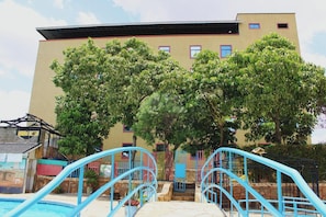 A building with a swimming pool, blue stairs, and trees in front. - Global Hotels & Suites Kitengela (Kitengela)