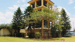 A two-story building with a yellow facade and a red roof, surrounded by tall trees and a grassy lawn. - Global Hotels & Suites Kitengela (Kitengela)
