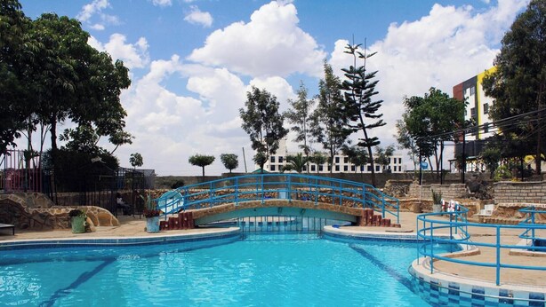A swimming pool with a blue spiral staircase leading to a bridge over the water. - Global Hotels & Suites Kitengela (Kitengela)