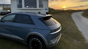 Een moderne auto geparkeerd voor een gemoderniseerde stacaravan met uitzicht op de zonsondergang.