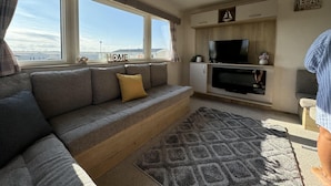 Een moderne woonkamer met een grijze bank, een flatscreen televisie en een open haard.