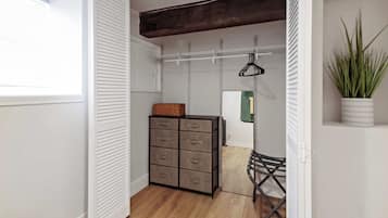 Un armario vestidor con suelo de madera, una estantería metálica y una planta en maceta.