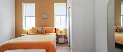 A bedroom with a large bed, two bedside tables with lamps, a mirror, and a bench.