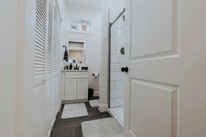 Een smalle gang met witte deuren, een kleine badkamer met toilet en een douchehoek.
