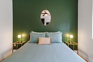 A bedroom with a bed, two bedside tables with lamps, a ceiling fan, and a wall-mounted mirror. - Soulard 4BR Near Busch & Arch — Private Patio, Fast Wi-Fi, Easy Parking (St. Louis)