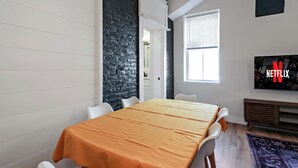 Quarto com mesa de jantar, cadeiras brancas, parede de tijolos pretos, uma janela e um sinal da Netflix.