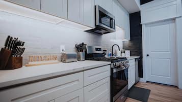 A modern kitchen with white cabinets, a microwave, a toaster, and a stove.