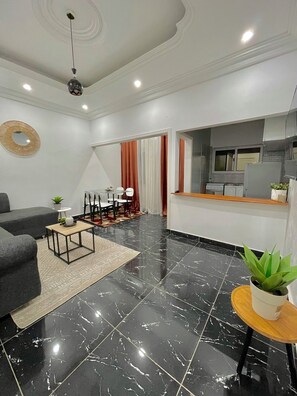 A modern living room with a black marble floor, a grey sofa, a wooden coffee table, and a dining area with chairs and a table. - Appartements VEKA (Pointe-Noire)