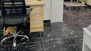 A modern office space with a black office chair, a wooden desk, and a potted plant. There are three framed pictures on the wall depicting cityscapes. - Appartements VEKA (Pointe-Noire)
