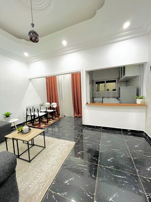 A modern living room with a dining area, black marble flooring, and a kitchen visible through an open door. - Appartements VEKA (Pointe-Noire)