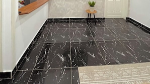 A modern interior with a black marble floor, a mounted TV, a small potted plant, and a white door. - Appartements VEKA (Pointe-Noire)