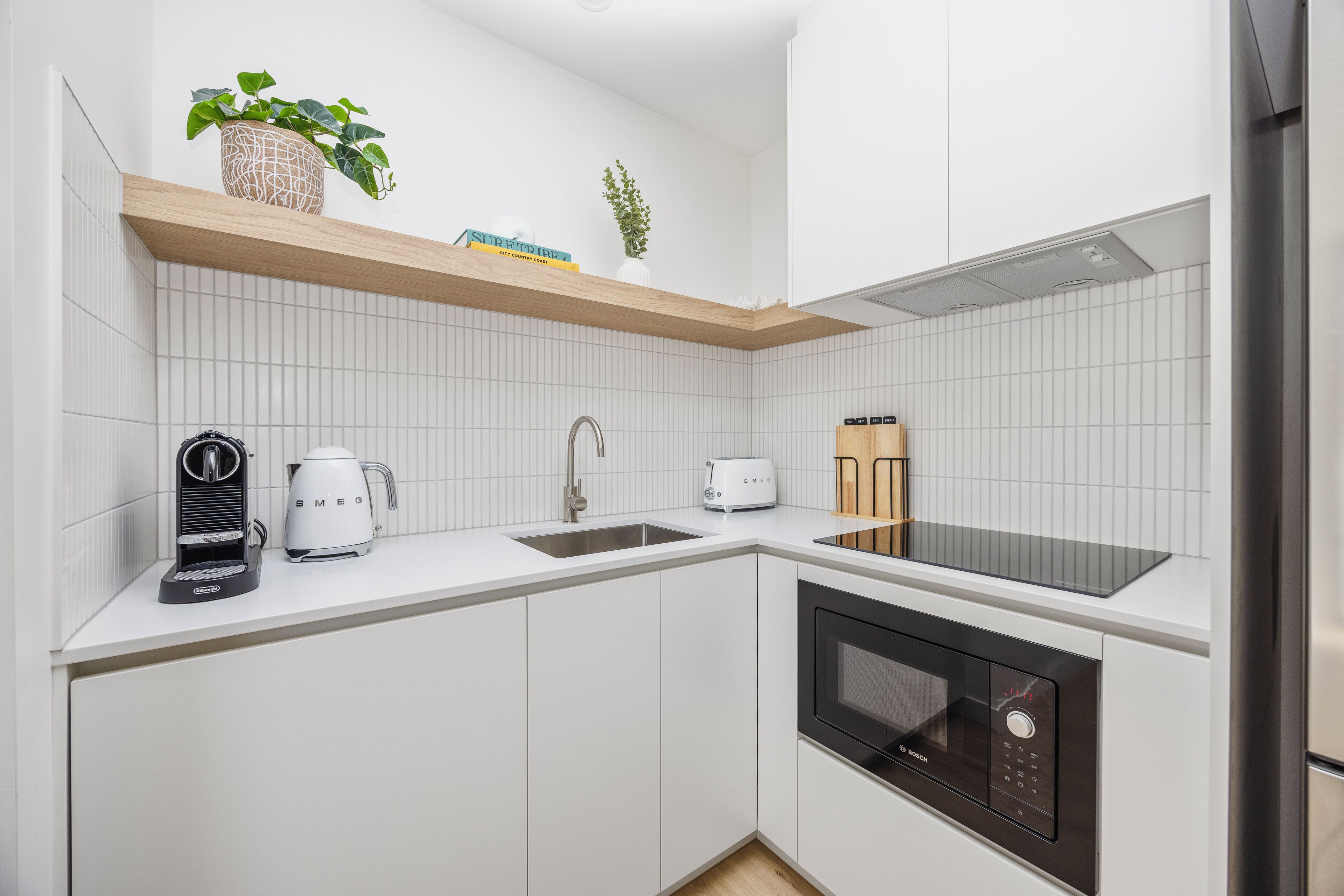 Una cocina moderna con armarios blancos, horno empotrado, cafetera y tostadora.