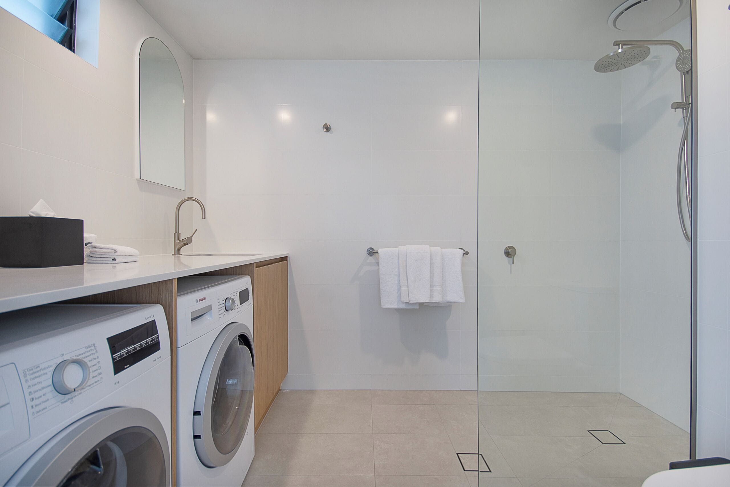 Uma casa de banho moderna com máquina de lavar roupa, lavatório, espelho e cabine de duche com vidro.
