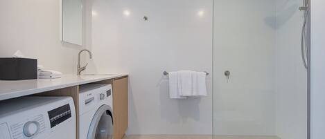 Uma casa de banho moderna com máquina de lavar roupa, lavatório, espelho e cabine de duche com vidro.