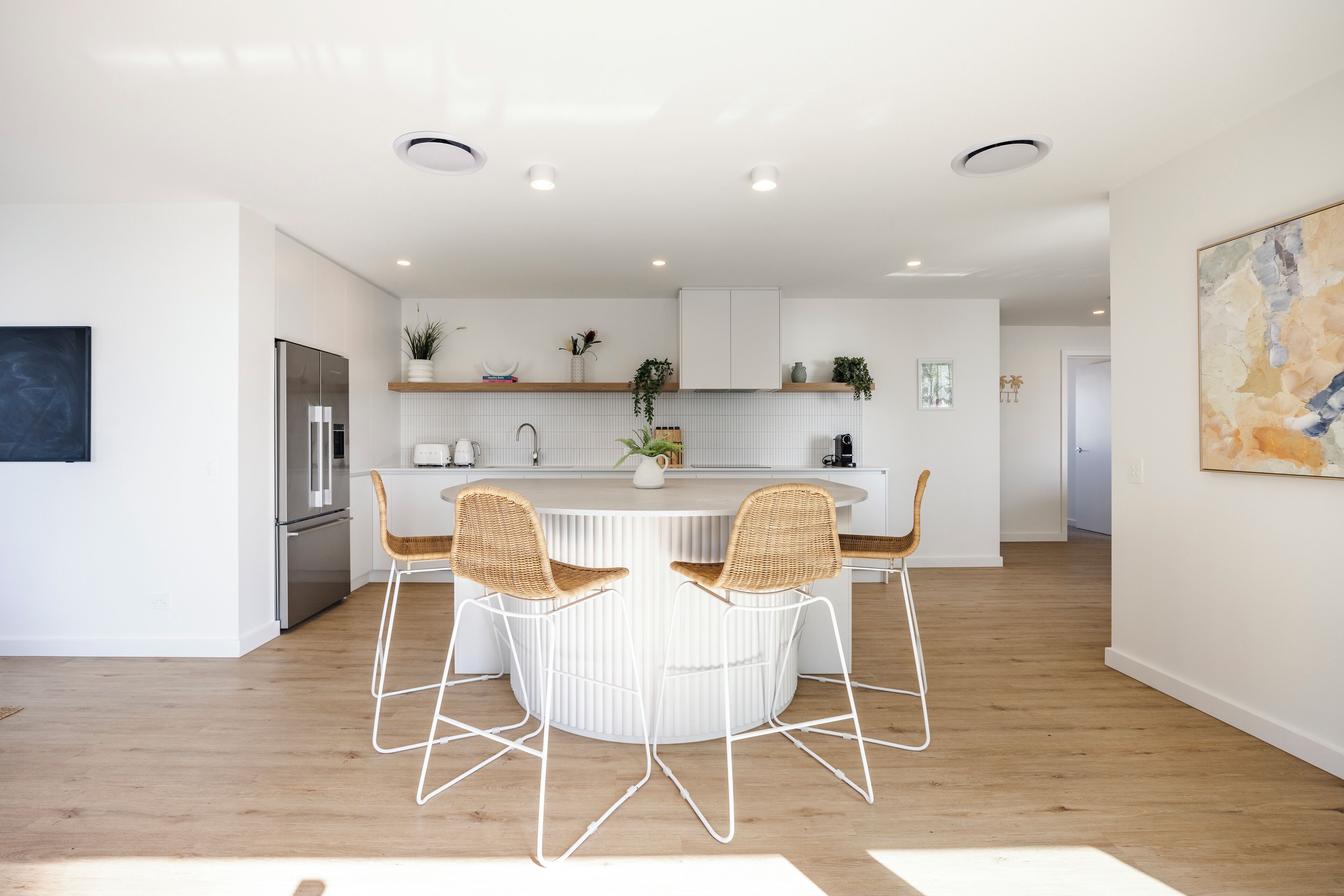 A modern kitchen with white cabinetry, a central island with chairs, and a refrigerator.