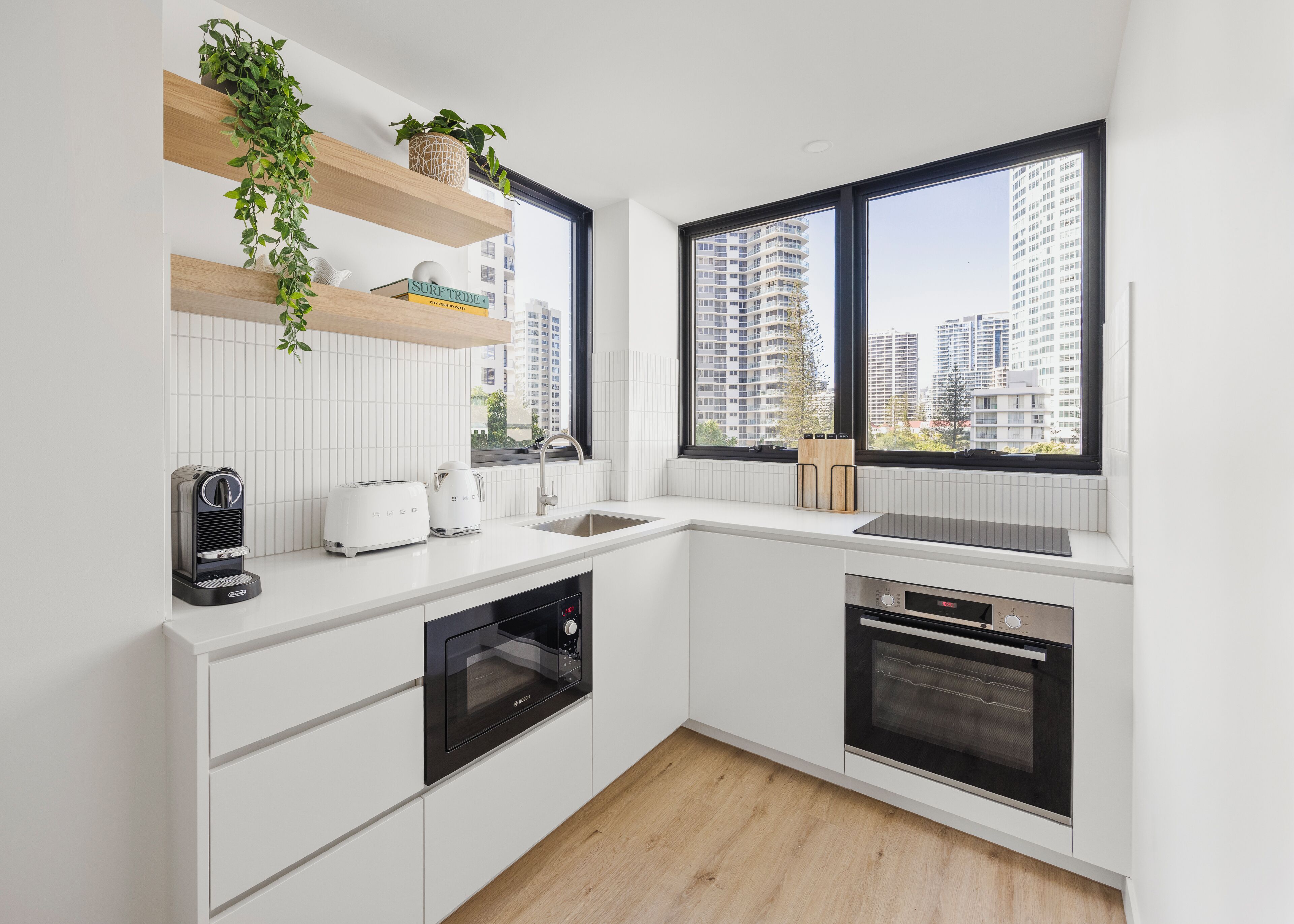 A modern kitchen with white cabinetry, a built-in oven, a dishwasher, and a window with a city view.
