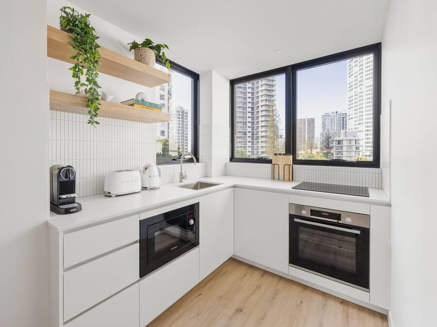 A modern kitchen with white cabinetry, a built-in oven, a dishwasher, and a window with a city view.