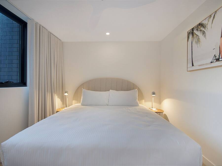 A hotel room with a large bed, a window with curtains, a headboard, and a wall-mounted artwork.