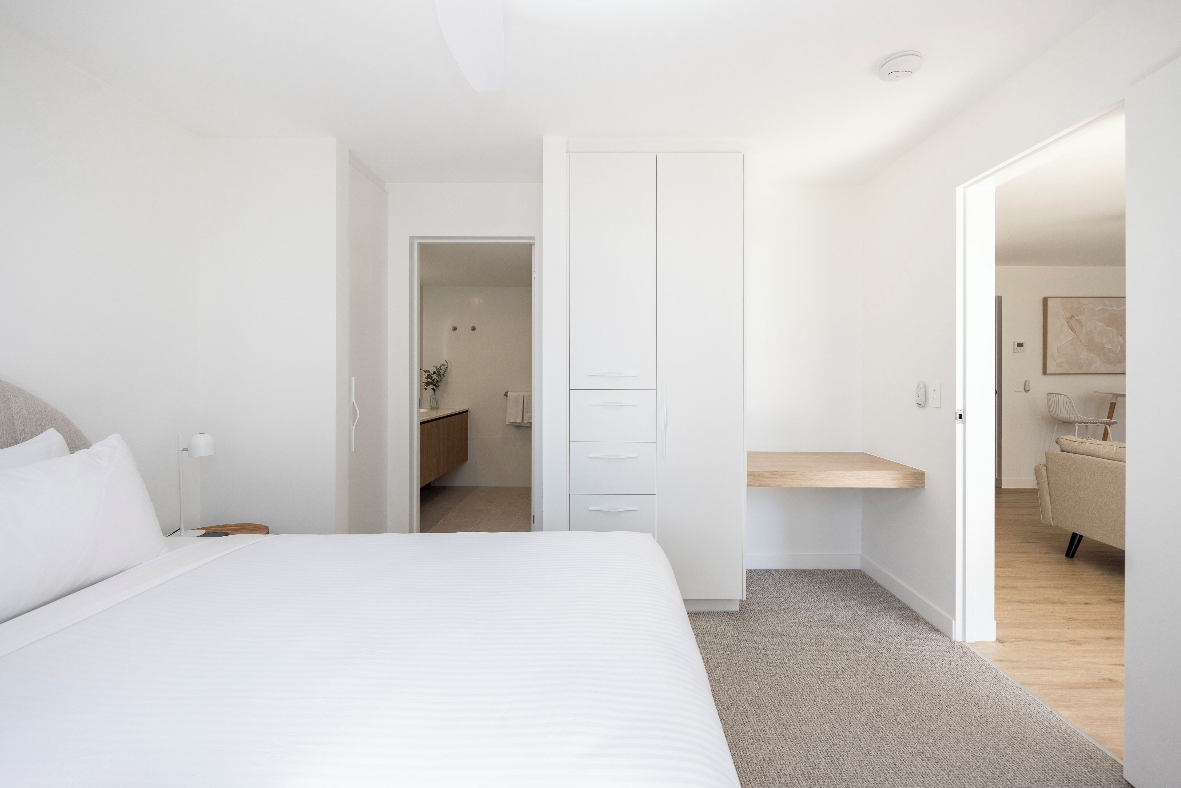 Une chambre à coucher moderne avec un grand lit, une table de chevet, une armoire et un petit espace bureau.