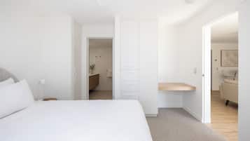 A modern bedroom with a large bed, a bedside table, a wardrobe, and a small desk area.
