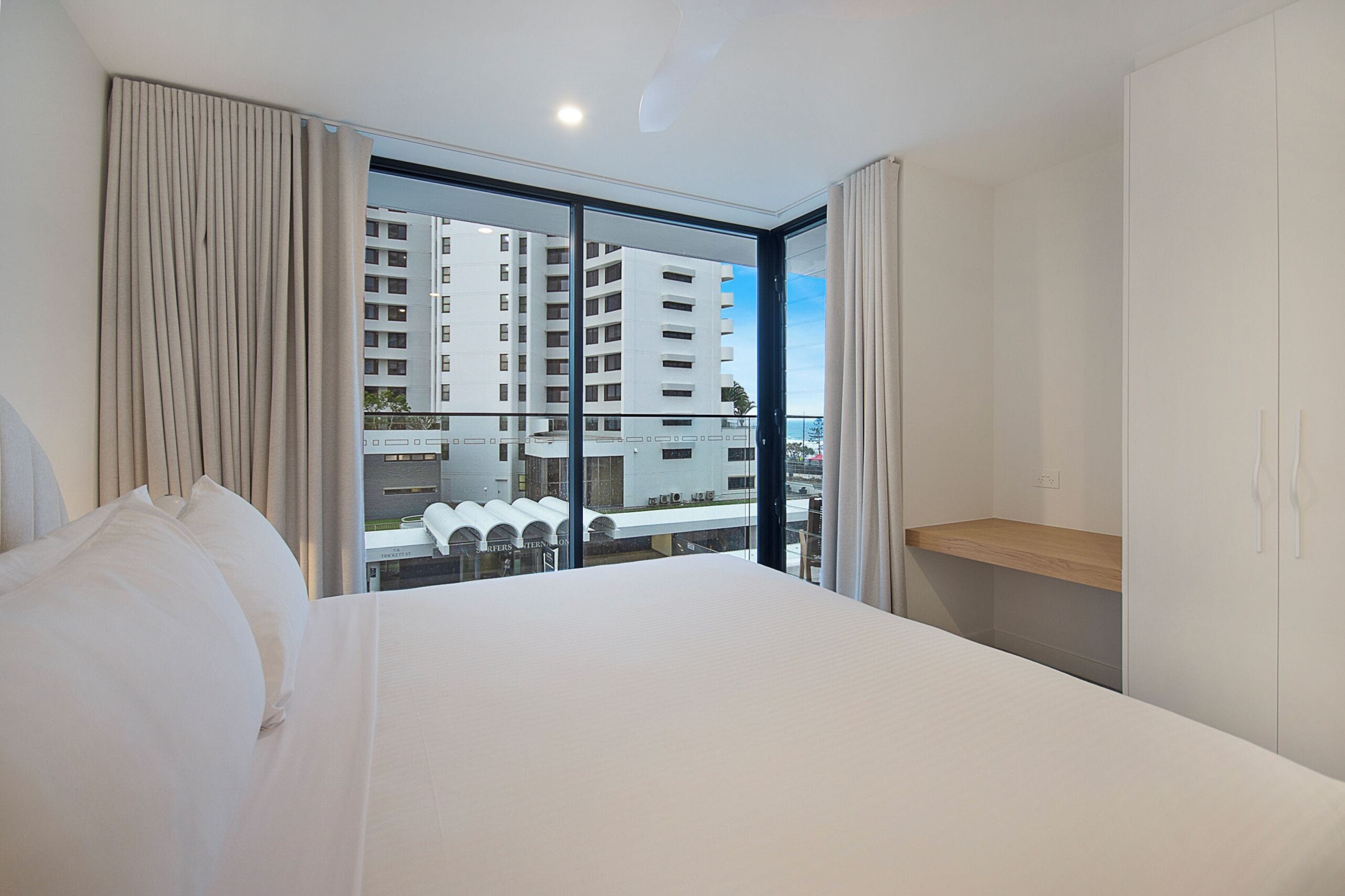 Una habitación de hotel moderna con una cama grande, una estantería de madera y vistas a un rascacielos.