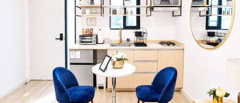 A modern kitchen with built-in appliances, a round mirror, and a dining area with two blue chairs.
