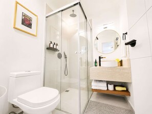 Une salle de bain moderne avec une douche à parois de verre, des toilettes blanches et un lavabo avec un miroir au-dessus.