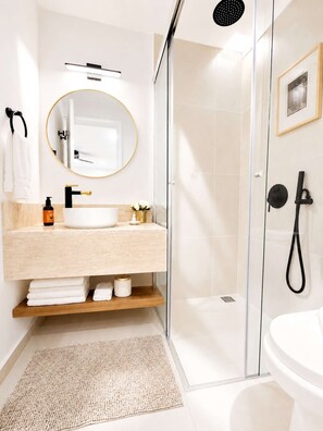 Un baño moderno con cabina de ducha de vidrio, espejo redondo, lavabo blanco y retrete.