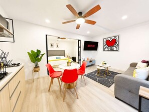 Un salon moderne comprenant un coin repas, un canapé gris, un téléviseur et un ventilateur de plafond.