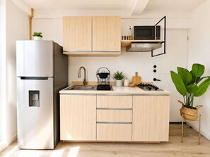 Una cocina moderna con refrigerador de acero inoxidable, gabinetes de madera, microondas, estufa a gas y un lavamanos.
