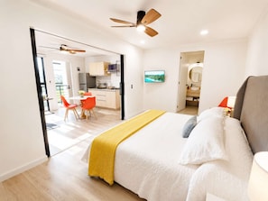 Een moderne slaapkamer met een bed, een plafondventilator en uitzicht op de keuken.