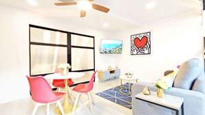Un salon moderne doté d’un ventilateur de plafond, d’un téléviseur, d’un canapé, d’une table à manger avec des chaises et d’une grande fenêtre avec des stores.