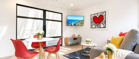 A modern living room with a dining area, a sofa, a TV, and artwork on the walls.