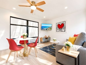 Een moderne woonkamer met een eethoek, een bank, een televisie en kunstwerken aan de muur.