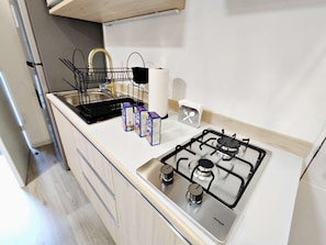 Une cuisine de taille réduite, équipée d’une cuisinière à gaz, d’un évier et d’un égouttoir à vaisselle.