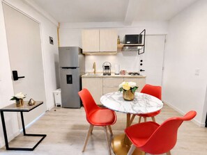 A compact kitchen with a refrigerator, sink, and stove. There is a dining table with chairs and a vase of flowers.