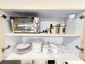 Kitchen pantry with a toaster oven, plates, bowls, mugs, and glasses.