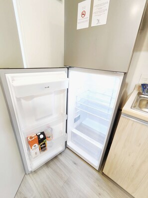 Modern kitchen with refrigerator, stainless steel sink, and light-colored cabinetry.