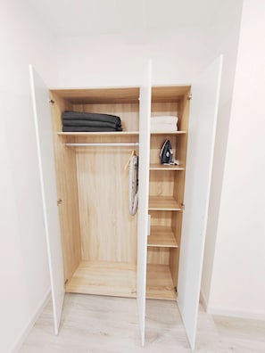 Un dressing avec des étagères en bois, une tringle et une planche à repasser pliable.