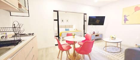 A modern kitchen with a built-in stove, a dining area with a round table and red chairs, a ceiling fan, and a TV mounted on the wall.