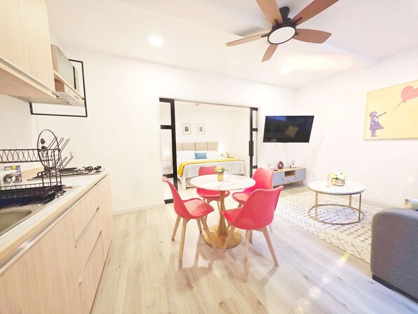 A modern kitchen with a built-in stove, a dining area with a round table and red chairs, a ceiling fan, and a TV mounted on the wall.