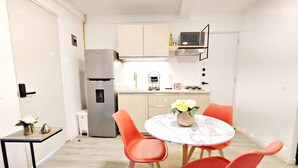 Une cuisine compacte équipée d’un réfrigérateur, d’un four à micro-ondes et d’un évier. On y trouve une table à manger avec quatre chaises et un vase de fleurs.