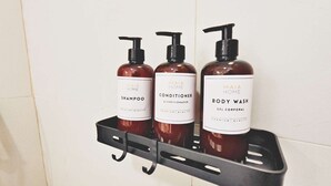 A bathroom shelf with three bottles of Maia Home products: shampoo, conditioner, and body wash.