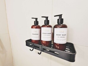A bathroom shelf with three bottles of Maia Home products: shampoo, conditioner, and body wash.