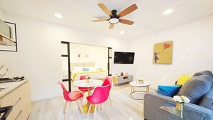 A modern hotel room with a dining area, a sofa, a TV, and a ceiling fan.