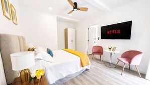 Habitación de hotel moderna con cama, mesita de noche, lámpara y televisor empotrado mostrando 'NETFLIX'.