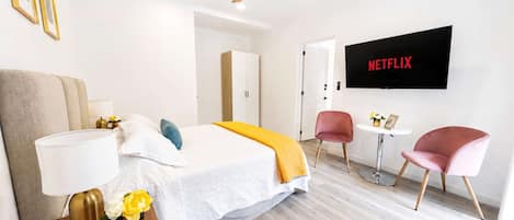 A modern hotel room with a bed, bedside table, lamp, and a wall-mounted TV displaying 'NETFLIX'.
