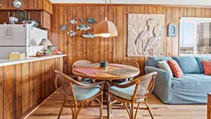 Una cocina acogedora con paneles de madera, un rincón de comedor con sillas de mimbre y un sofá azul con cojines.